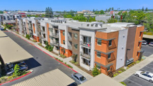 aerial exterior of residential building, private patios, covered parking available, three-story walk-up. Photo Taken on a sunny day.