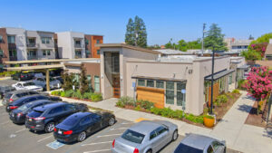 Aerial Exterior of Leasing Office, Meticulous landscaping around building, parking out front, residential buildings in background, covered parking available.