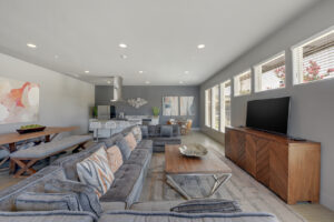 Interior Clubhouse, Large Sectional Couch, Tv on entertainment center, large coffee table, large dining table behind sectional, kitchen area in back of room, contemporary design and art on walls.