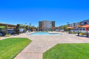 Exterior Enclosed Swimming Pool area, bistro tables with umbrellas, grill area in corner of enclosure, lifeguard chair.
