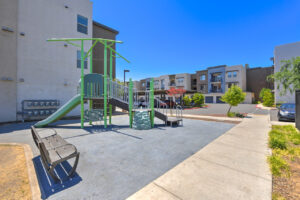Exterior Playground, Soft landing pad, slides, bench along playground, buildings in background.