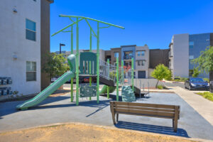 Exterior Playground, soft landing pad, bench along playground, parking nearby, residential buildings in background.