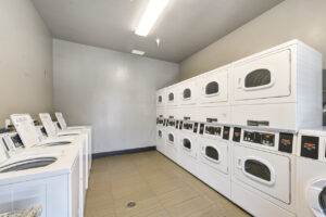 Interior Laundry Facilities, four washers in view, 11 dryers in view, tile floor, neutral toned walls, granite countertops.