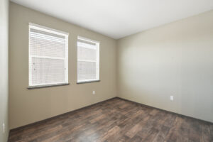 Interior Unit Living Room, Neutral toned walls, wood-like floors, two windows.