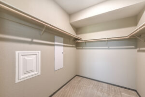 Interior Unit walk-in Closet, Electrical panel in closet, multiple shelves for clothes storage and hanging, Neutral toned walls and carpeting.