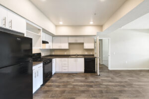 Interior Unit Kitchen, Open Floor Plan, wood-like Floors, black appliances, dual stainless steel sink, white cabinetry.