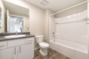 Interior Unit Bathroom, Double sink vanity, drank brown laminate countertop, white appliances, wood-like floors, white cabinetry, shower/bathtub.